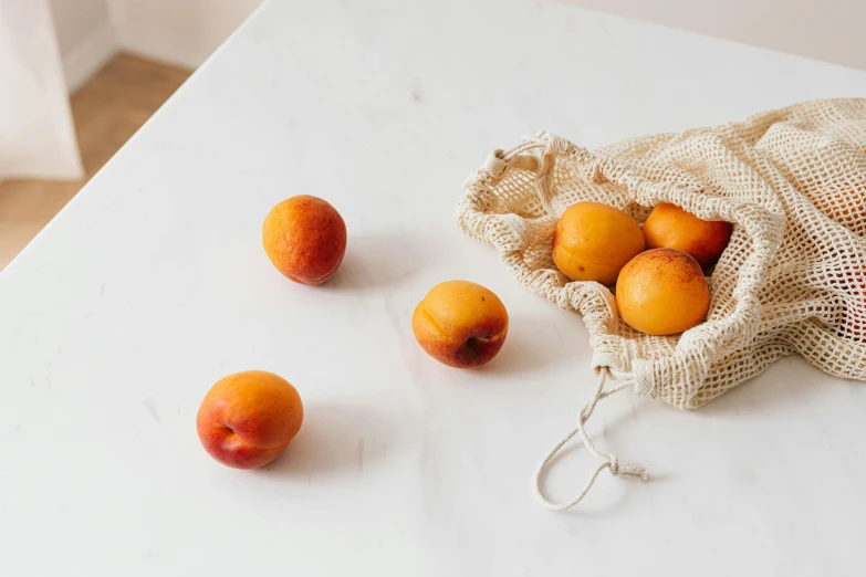 a bag of apricots sitting on top of a table, a still life, unsplash, background image, white marble interior photograph, various posed, uncropped