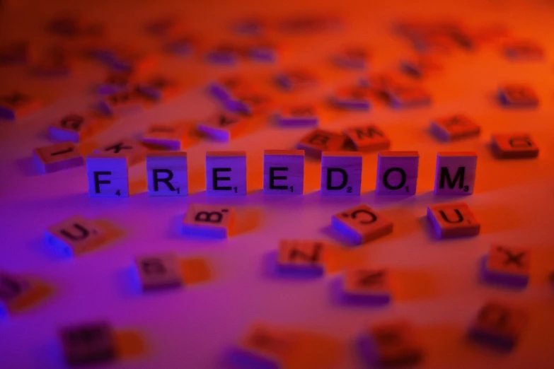 the word freedom spelled in scrabbles on a table, an album cover, by Niko Henrichon, trending on pixabay, figuration libre, light red and deep blue mood, some orange and purple, taken in the night, profile picture 1024px