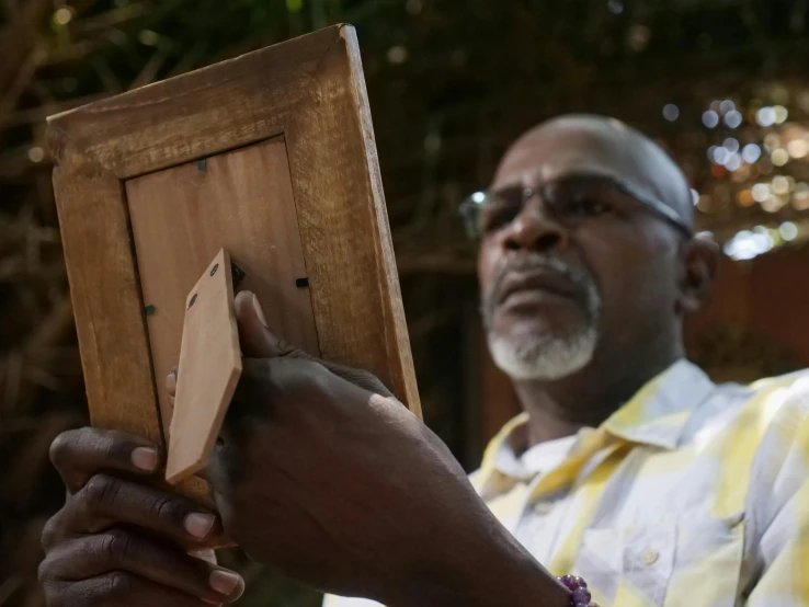 a man holding a piece of wood in his hand, a picture, visual art, emmanuel shiru, center frame medium shot, profile image, slide show