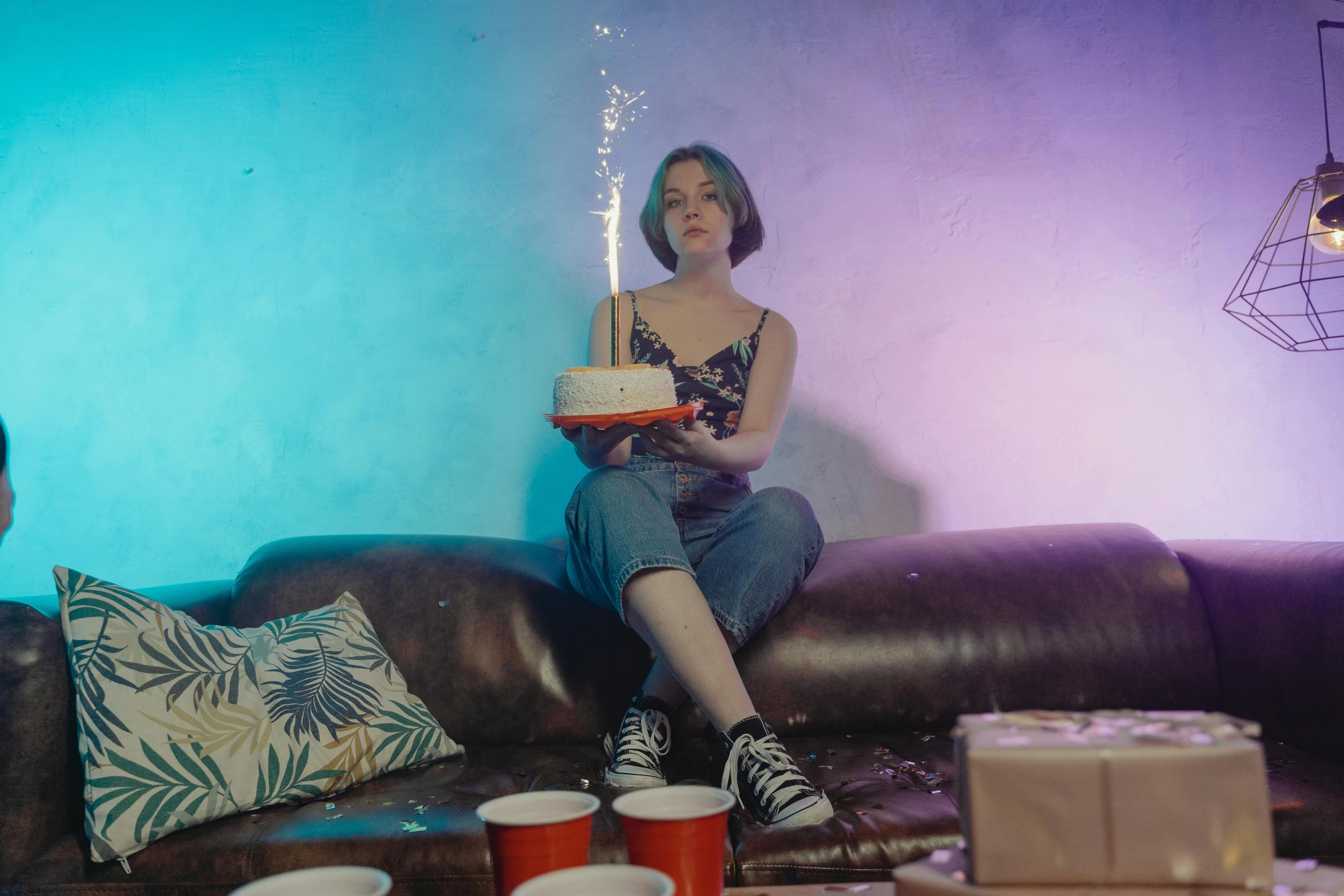 a woman sitting on a couch holding a birthday cake, inspired by Elsa Bleda, pexels contest winner, graffiti, maisie williams, pyrotechnics, bisexual lighting, at a birthday party