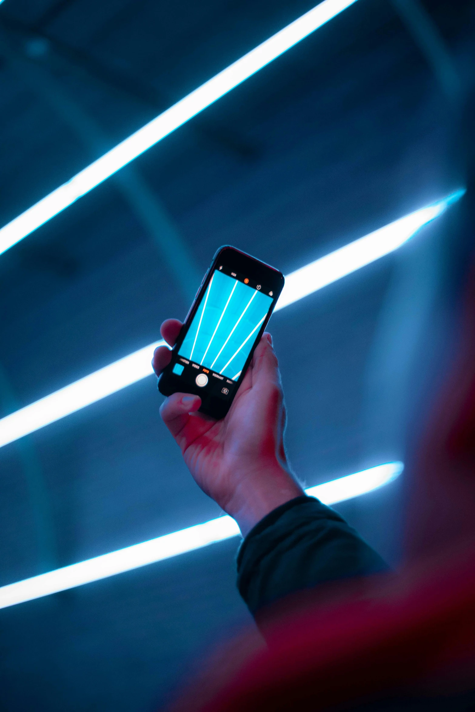 a person holding up a smart phone in front of neon lights, by Matthias Stom, teal color graded, geometric light rays, with a black background, a long-shot