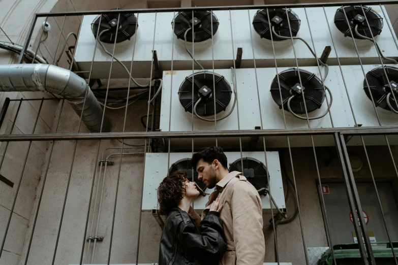 a man and a woman standing next to each other, a photo, by Emma Andijewska, pexels contest winner, air conditioner, background image, couple kissing, highly mechanical