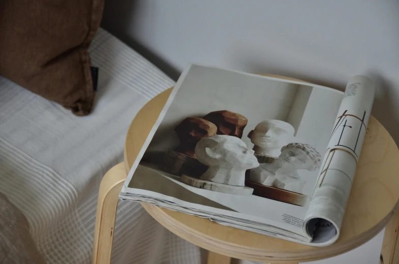 a magazine sitting on top of a wooden table, a marble sculpture, inspired by Sarah Lucas, unsplash, studyng in bedroom, photorealistic faces, wooden side table, high quality paper