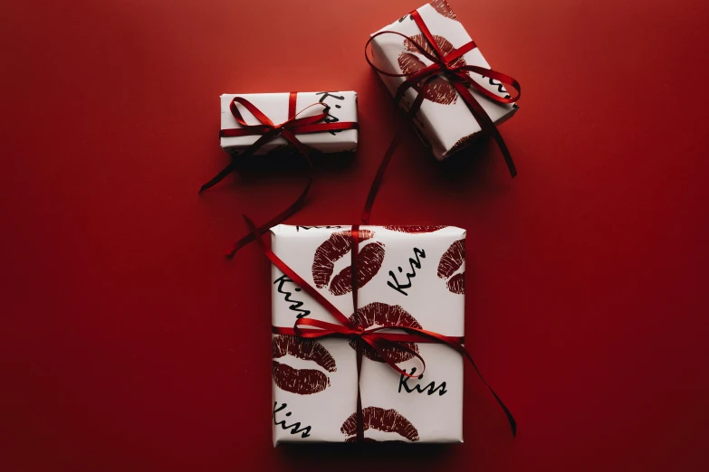 three wrapped presents on a red background, by Julia Pishtar, pexels contest winner, graffiti, luscious red lips, engraved, kiss, top angle view