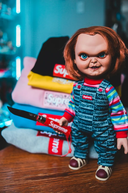 a doll sitting on top of a wooden table, a cartoon, inspired by Clark Voorhees, trending on pexels, lowbrow, in the bedroom at a sleepover, angry looking at camera, chucky, streetwear