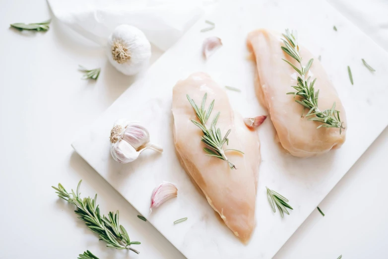 two pieces of chicken sitting on top of a cutting board, a photo, trending on pexels, herbs, silver，ivory, 6 pack, white backround