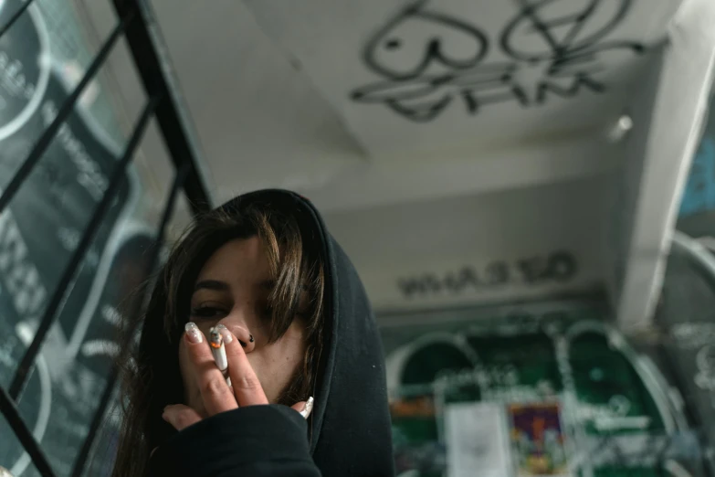 a woman in a black hoodie talking on a cell phone, inspired by Elsa Bleda, trending on pexels, graffiti, smoke under the ceiling, ganja, thoughtful ), low quality photo