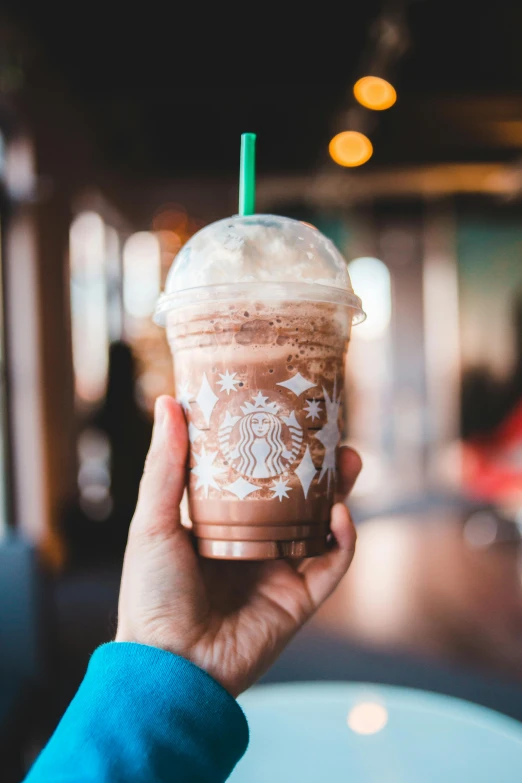 a person holding up a cup of coffee, a colorized photo, inspired by Elsa Bleda, trending on unsplash, happening, milkshake, starbucks, brown and cyan color scheme, made of glazed