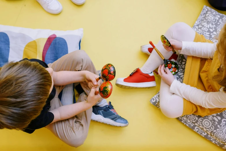 a couple of kids sitting on top of a floor, by Julia Pishtar, pexels contest winner, holding maracas, scarlet and yellow scheme, sneaker, activity play centre