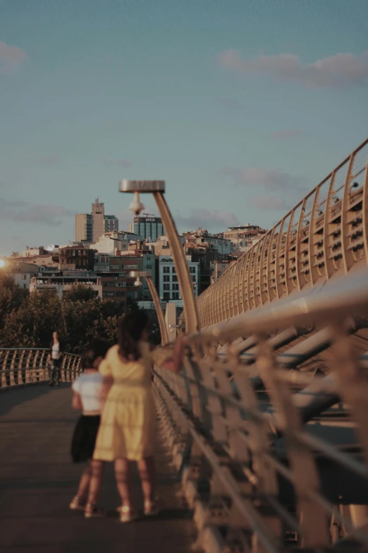 a couple of people walking across a bridge, by Modest Urgell, happening, golden hour cinematic, skyline showing, medium-shot, ::