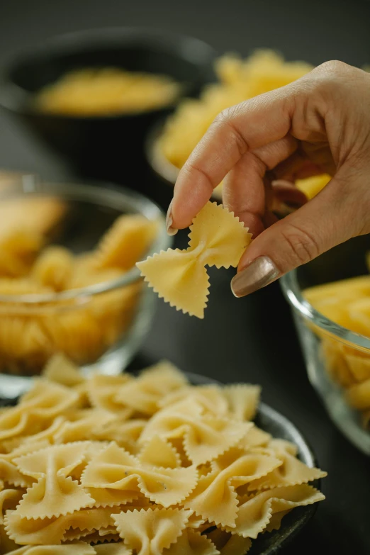 a person holding a piece of pasta in front of bowls of pasta, hands pressed together in bow, up-close, crisp clean shapes, straining