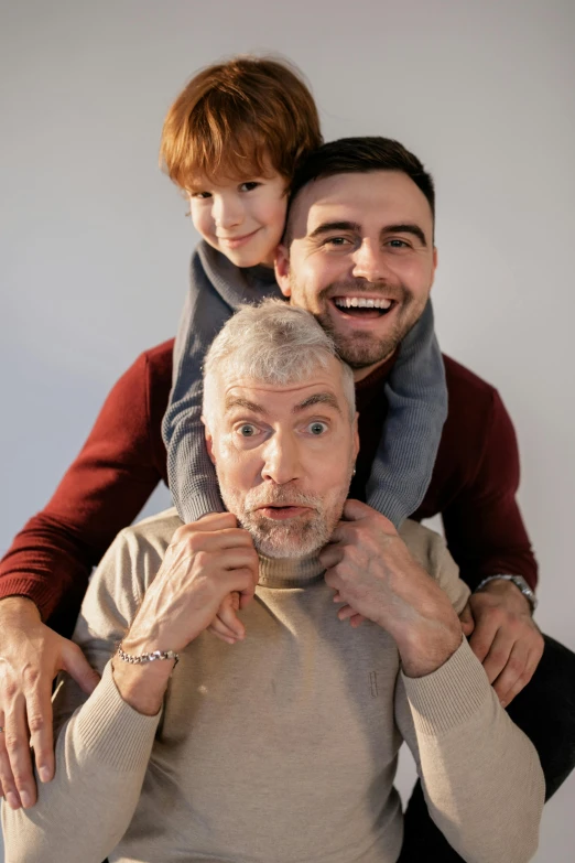 a man holding a little boy on his shoulders, a colorized photo, pexels, silver hair and beard, three heads, square masculine jaw, tall handsome guys