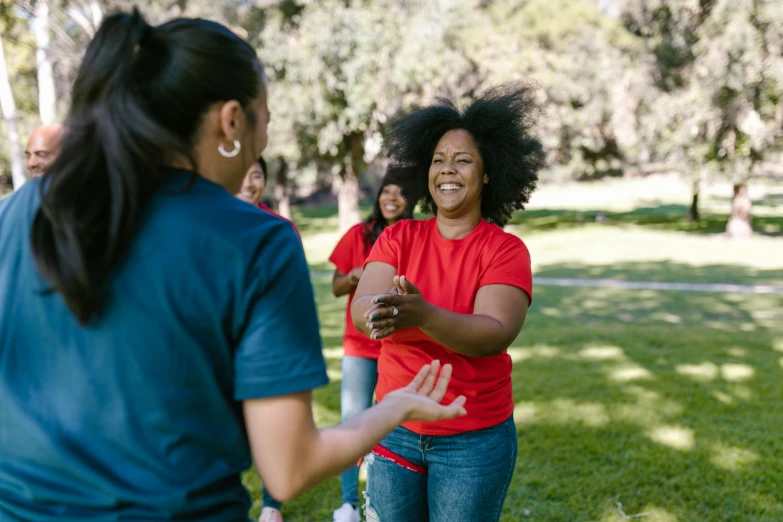 a couple of women standing on top of a lush green field, pexels contest winner, happening, playing games, of a family standing in a park, white t-shirt with red sleeves, african american young woman