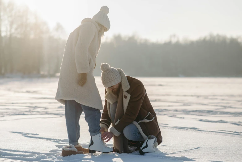 a couple of people that are standing in the snow, pexels contest winner, picnic, looking at the ground, brown, minna sundberg