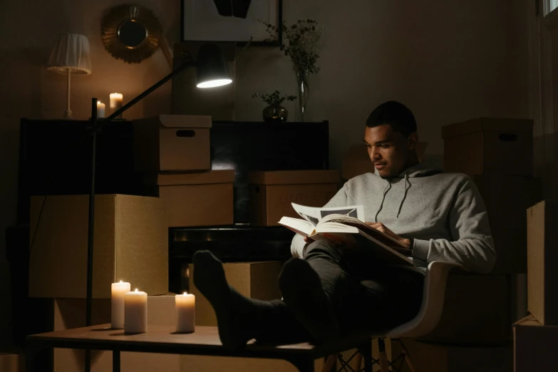 a man sitting in a chair reading a book, natural candle lighting, neutral lighting, studying, lights on