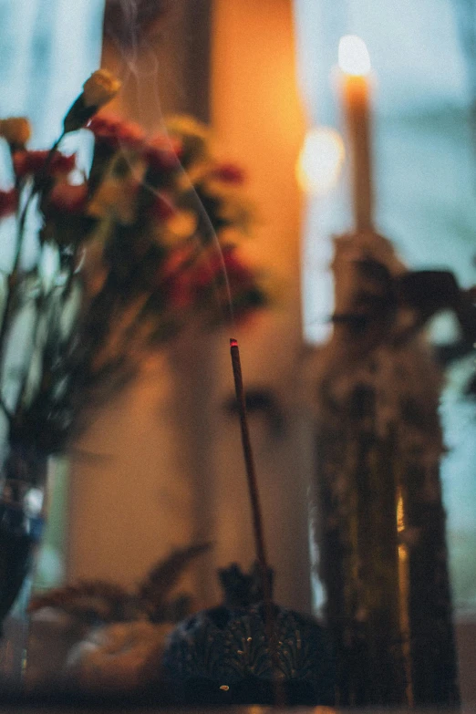 a candle sitting on top of a table next to a vase of flowers, by Elsa Bleda, unsplash, incense, blurred detail, shrine, multicoloured