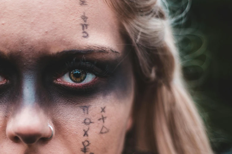 a close up of a woman with tattoos on her face, trending on pexels, lowbrow, covered in runes, black eye shadow, halloween, runic words