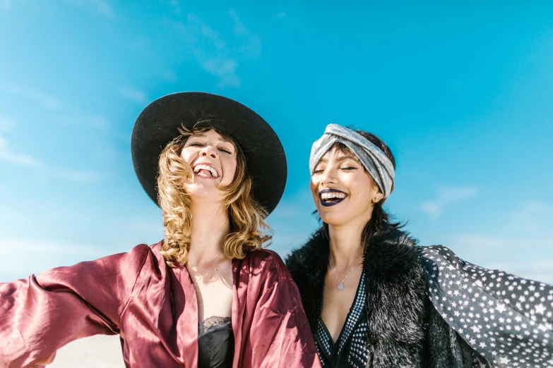 two women standing next to each other on a beach, a portrait, trending on pexels, happening, wearing a silly hat, laughing maniacally, avatar image, bohemian fashion