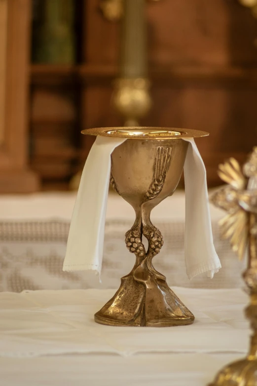 a gold chalicee sitting on top of a white table, on the altar, cloth and metal, lynn skordal, fine dining