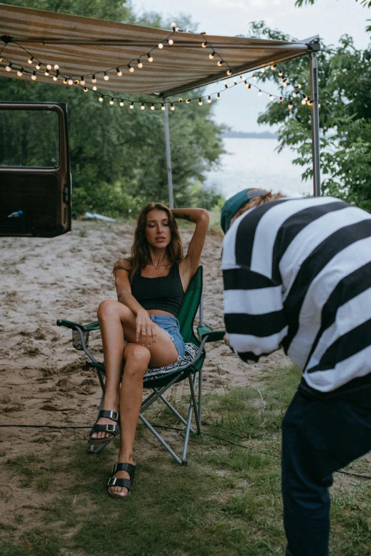 a woman sitting in a chair next to a man, unsplash contest winner, photorealism, camping, bikini model, on set, behind the scenes photo