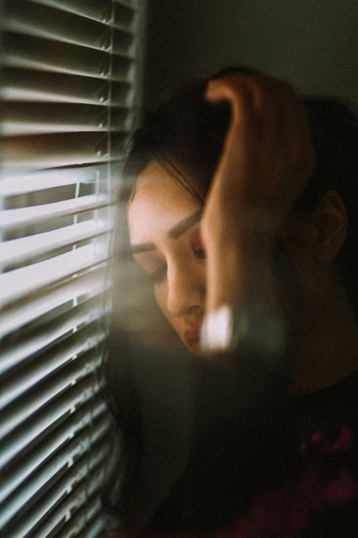 a woman standing in front of a window with blinds, a picture, inspired by Elsa Bleda, trending on pexels, realism, portrait of depressed teen, shy looking down, distorted, low quality photo