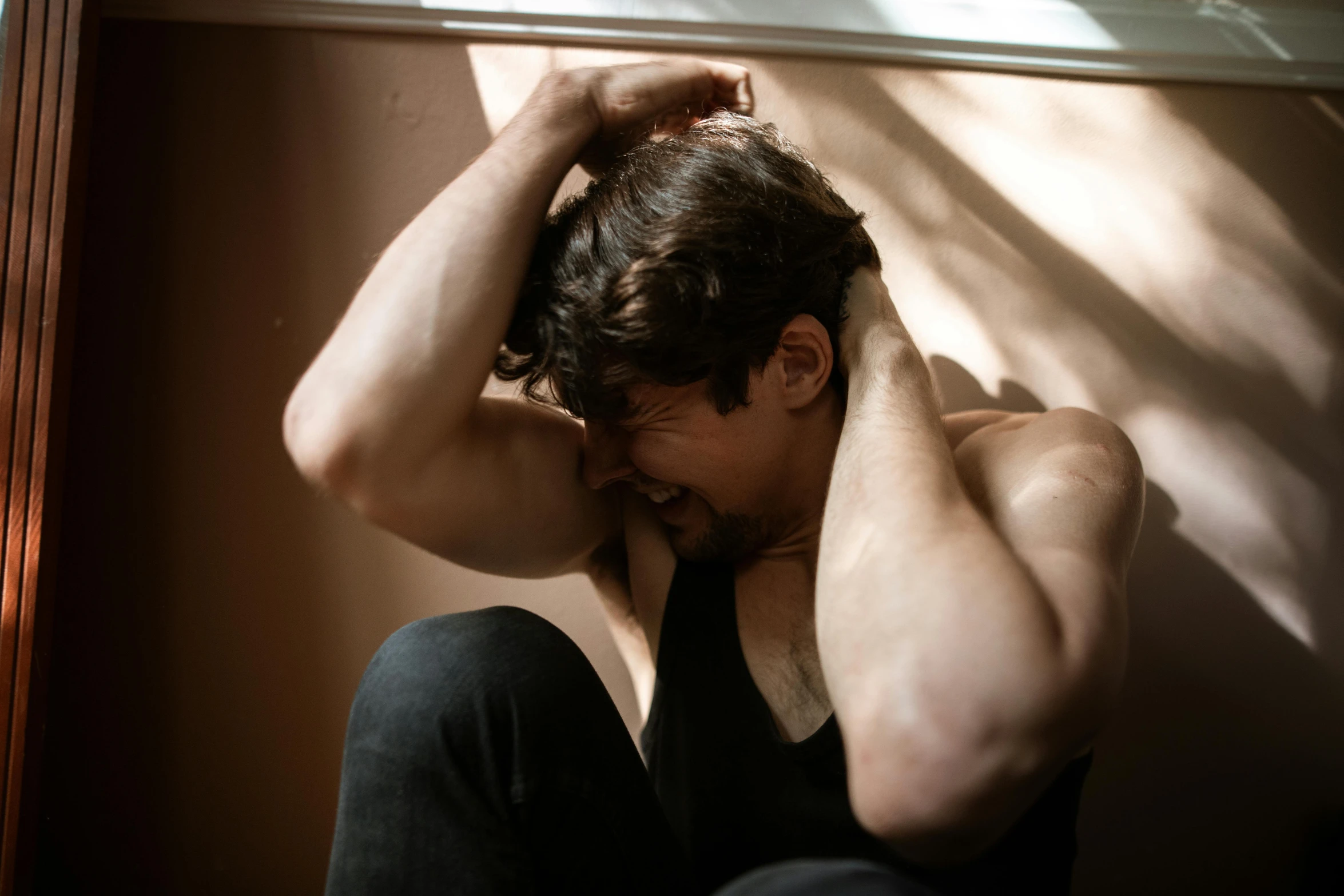 a man that is sitting down with his hands on his head, trending on pexels, depressed dramatic bicep pose, soft light, lachlan bailey, with a hurt expression