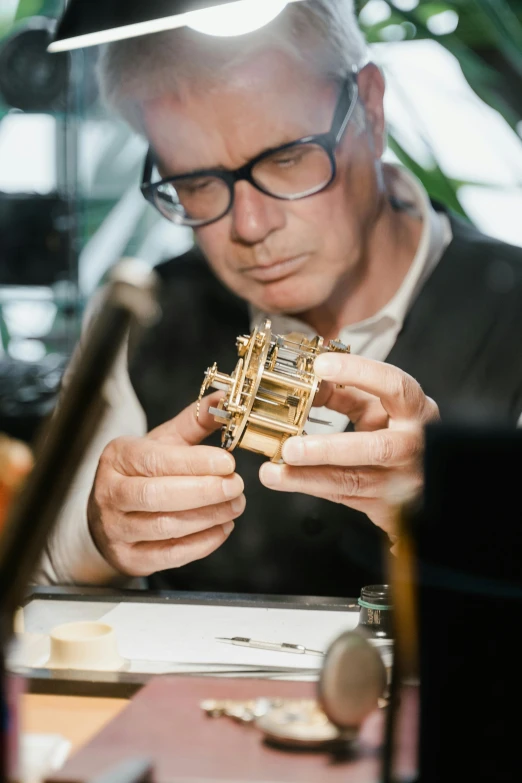 a man sitting at a table working on a wooden model, an engraving, by Matthias Stom, reddit, bauhaus, steampunk watch, gilt-leaf winnower, richard mille, with an intricate