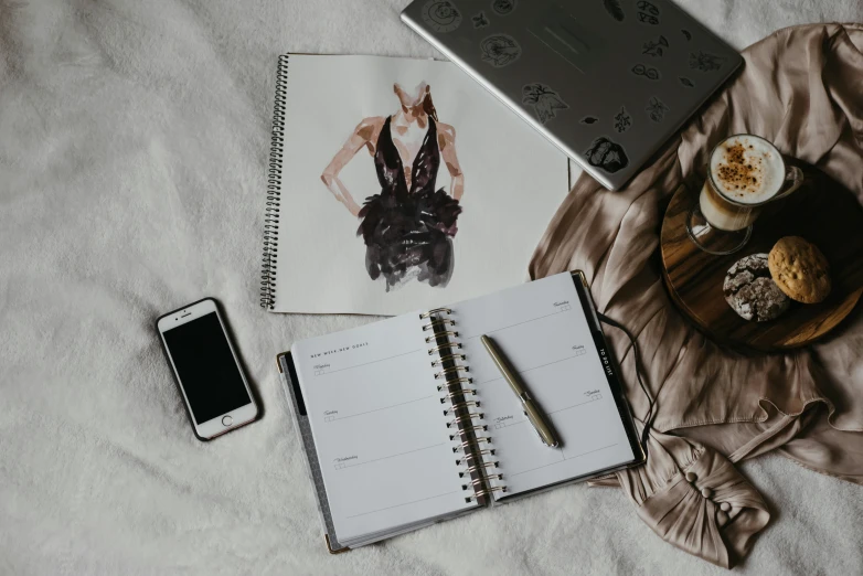 an open notebook sitting on top of a bed next to a cup of coffee, a sketch, by Emma Andijewska, trending on pexels, expensive outfit, thumbnail, shiny and metallic, portait photo