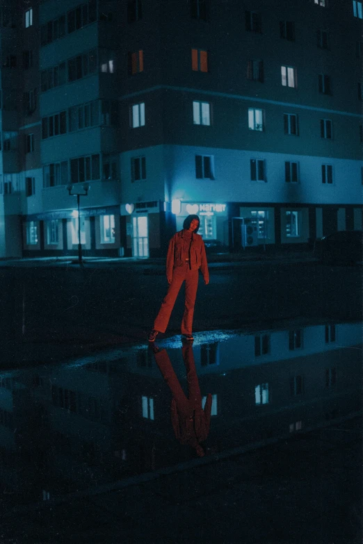 a person standing in front of a building at night, an album cover, inspired by Elsa Bleda, pexels contest winner, red suit, wearing a track suit, more reflection, gif