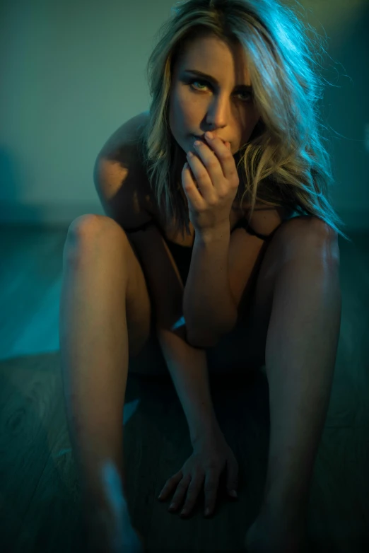 a woman sitting on the floor in a dark room, inspired by Elsa Bleda, pouting, blue lights, sydney sweeney, blonde