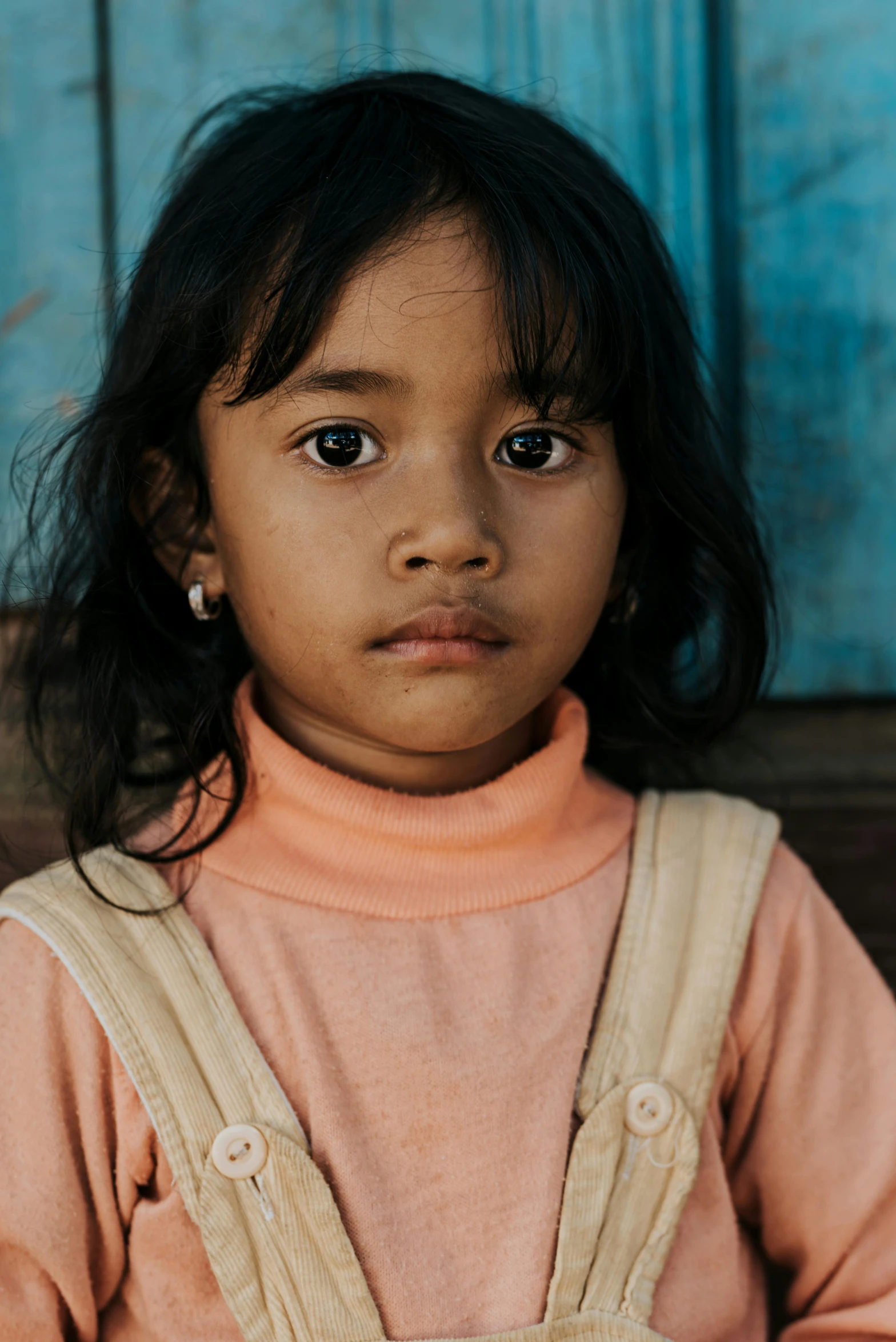 a little girl standing in front of a blue door, by Jesper Knudsen, pexels contest winner, sumatraism, serious face, square, she has olive brown skin, panoramic view of girl