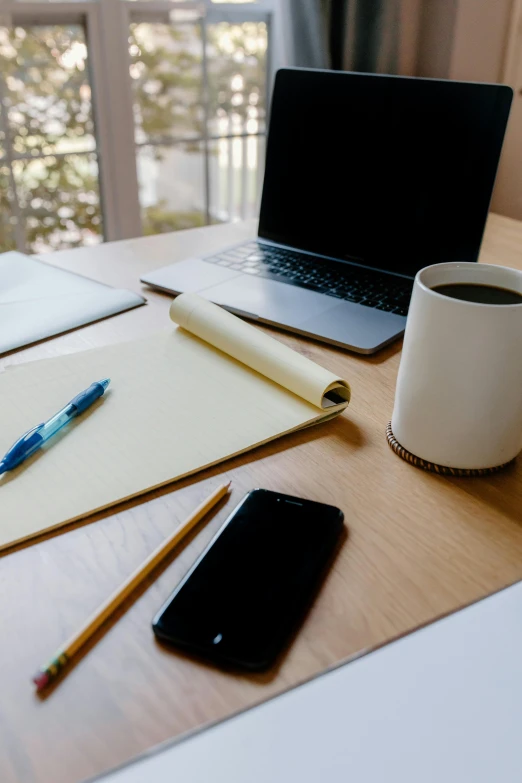 a laptop computer sitting on top of a wooden desk, pencil and paper, table in front with a cup, circular, curated collections