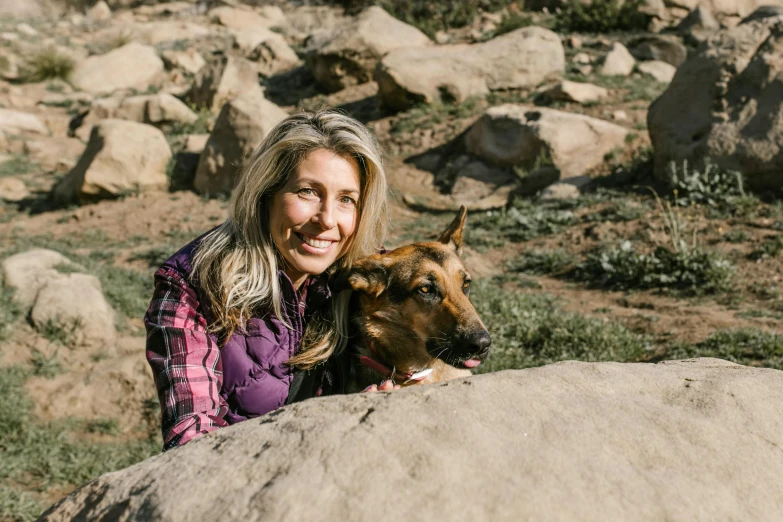 a woman sitting on top of a large rock next to a dog, a portrait, by Kristin Nelson, pexels contest winner, smiling at camera, avatar image, kim wexler and saul goodman, profile image