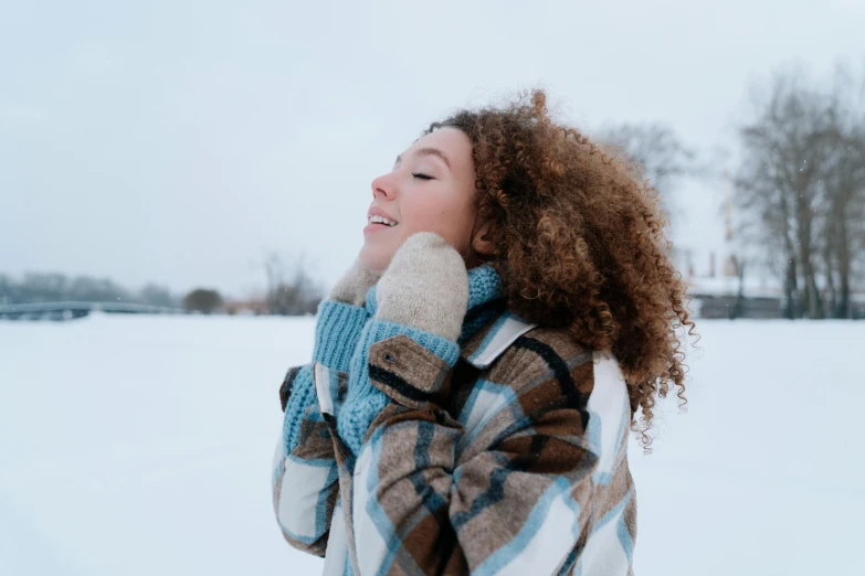 a woman with curly hair standing in the snow, trending on pexels, brown, having a good time, freezing blue skin, arm around her neck