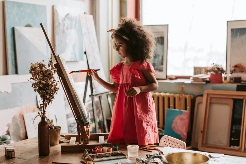 a little girl that is standing in front of a easel, by Julia Pishtar, pexels contest winner, light skinned african young girl, mate painting, girl wears a red dress, art workstation