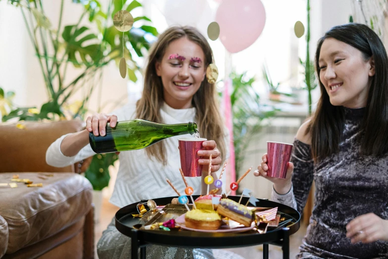 a couple of women sitting next to each other at a table, by Julia Pishtar, pexels contest winner, happening, pals have a birthday party, champagne on the table, teenage no, pink