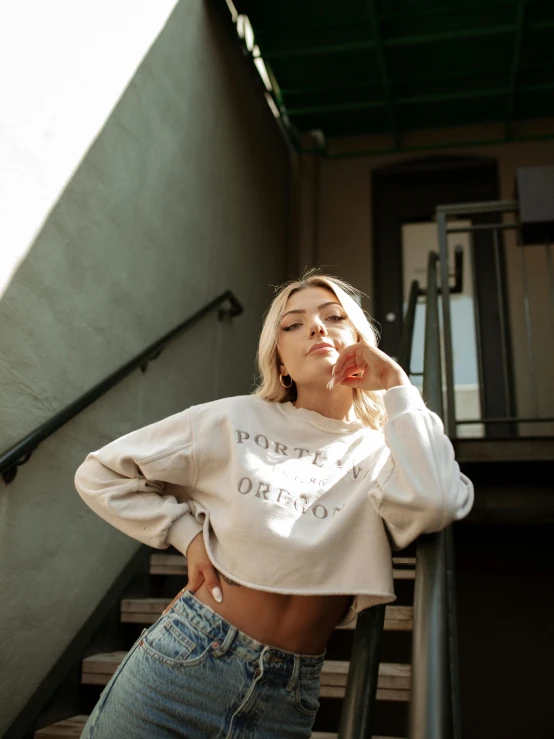 a woman standing on a set of stairs smoking a cigarette, inspired by Károly Lotz, trending on pexels, graffiti, wearing a cropped tops, wearing casual sweater, blonde cream, satisfied pose