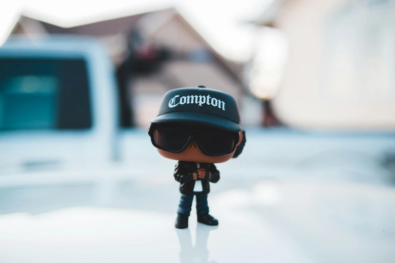 a close up of a toy on the hood of a car, a cartoon, by Tom Carapic, unsplash contest winner, with rap cap on head, wearing shades, as a full body funko pop!, carrington