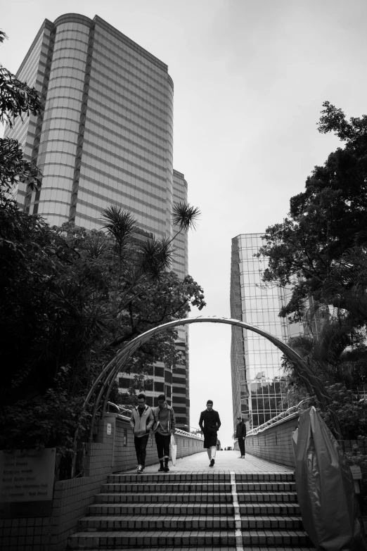 a group of people walking down a set of stairs, a black and white photo, inspired by Cheng Jiasui, unsplash contest winner, forest setting with skyscrapers, avenida paulista, big arches in the back, a man