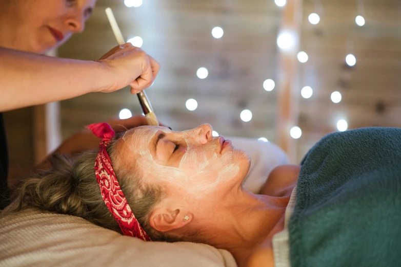 a woman getting a facial mask at a spa, by Julia Pishtar, unsplash, full of sand and glitter, skye meaker, white facepaint, rustic