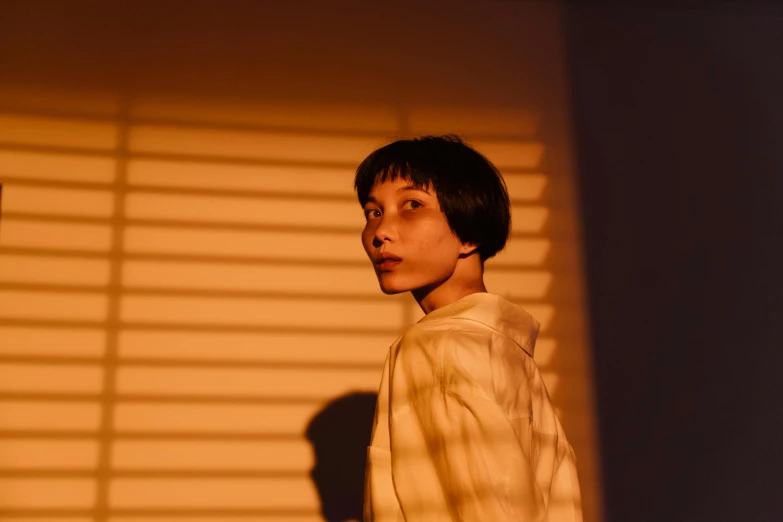a young man holding a nintendo wii game controller, an album cover, inspired by Elsa Bleda, pexels contest winner, realism, young asian woman, with short hair, portrait casting long shadows, orange light