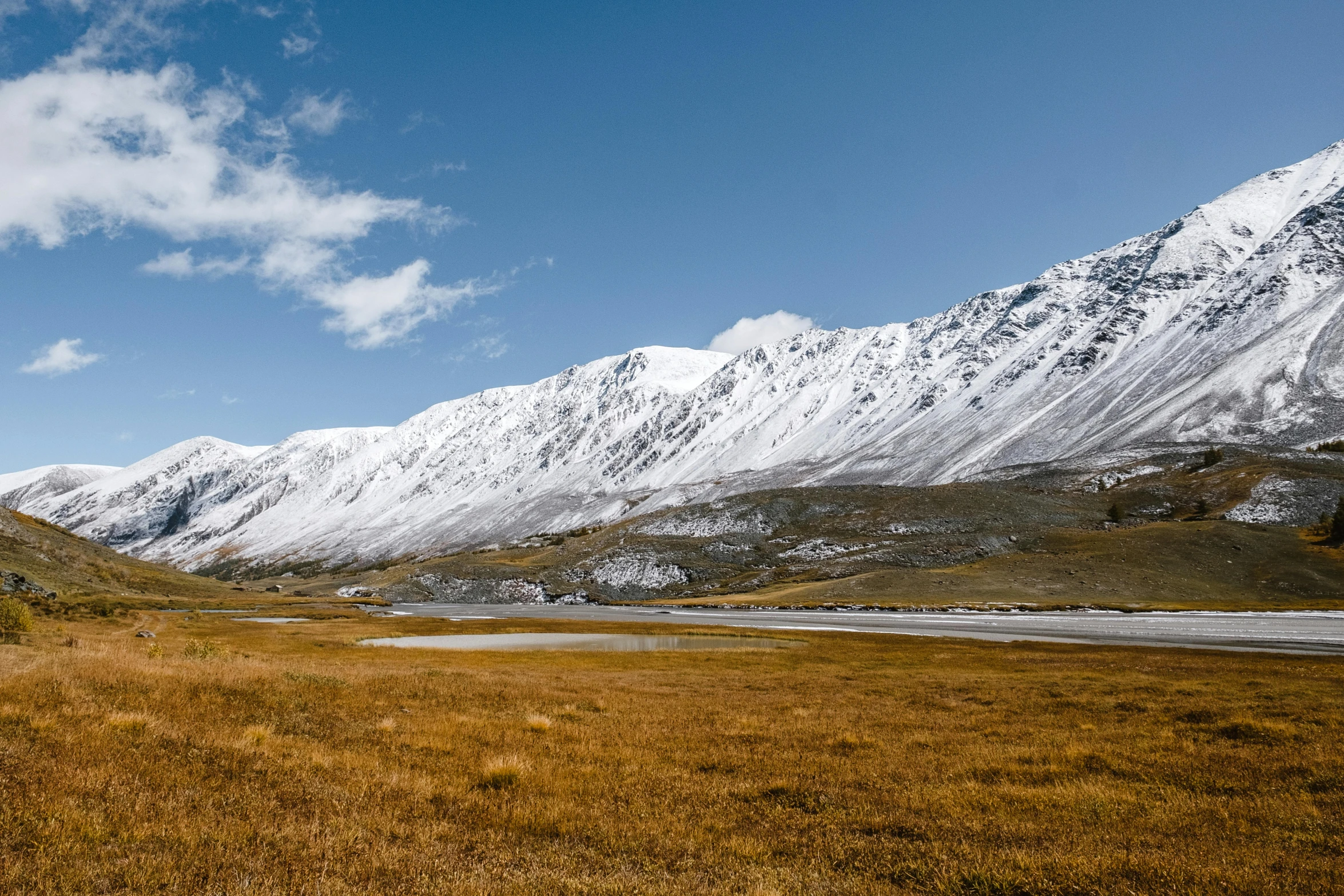 a grassy field with snow covered mountains in the background, by Muggur, pexels contest winner, hurufiyya, fall season, snowy arctic environment, gravel and scree ground, conde nast traveler photo