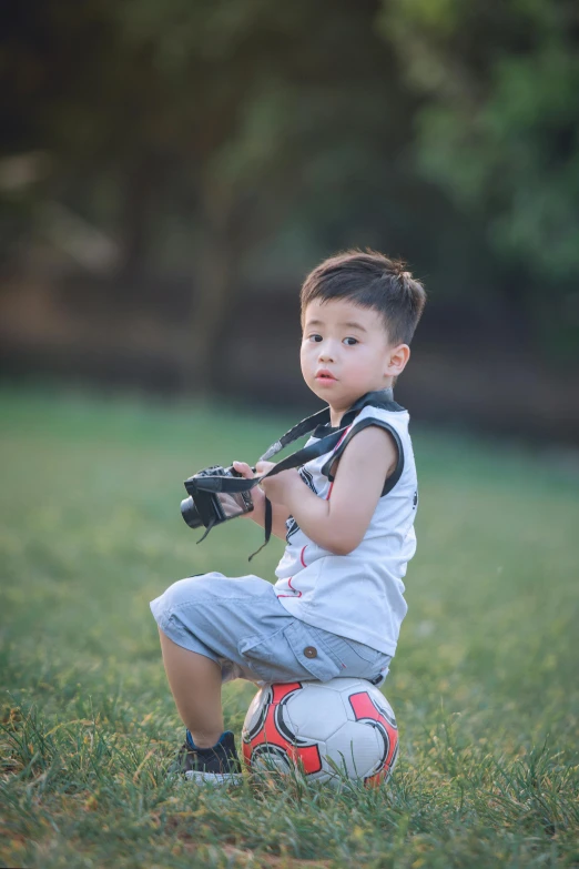 a young boy sitting on top of a soccer ball, a picture, by Reuben Tam, pexels contest winner, holding a camera, looking to his left, 15081959 21121991 01012000 4k, toys