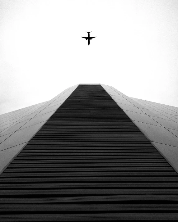 a black and white photo of an airplane flying over a building, by Brad Holland, unsplash contest winner, minimalism, space shuttle, museum photography, stairway to heaven, album cover