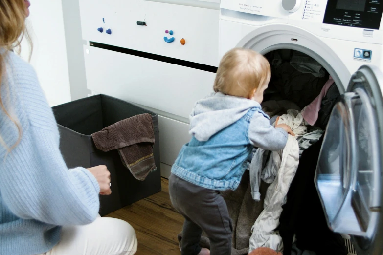 a woman holding a baby in front of a washing machine, by Alice Mason, pexels contest winner, people watching around, whealan, slide show, thumbnail