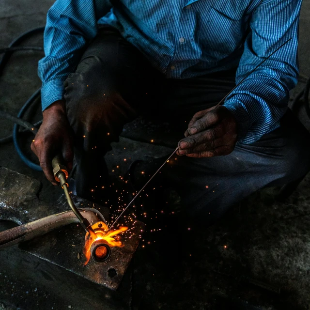 a man is working on a piece of metal, inspired by Afewerk Tekle, pexels contest winner, fire lit, india, photorealist, making love