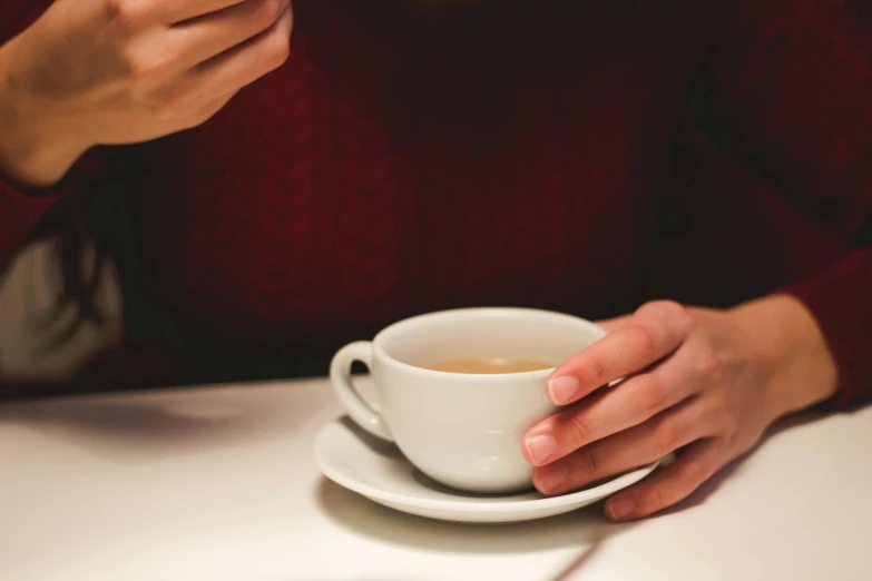 a woman sitting at a table with a cup of coffee, a photo, inspired by Richmond Barthé, trending on pexels, close-up of thin soft hand, soup, tea, middle close up