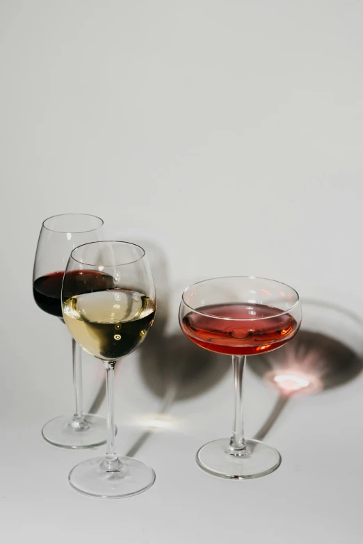 a couple of wine glasses sitting next to each other, with a drink, trio, on a pale background, glasses |