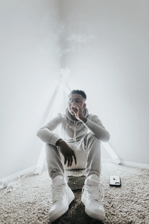 a man sitting on the ground talking on a cell phone, an album cover, inspired by Paul Georges, trending on pexels, white thick smoke, 2 1 savage, inside white room, intimidating pose