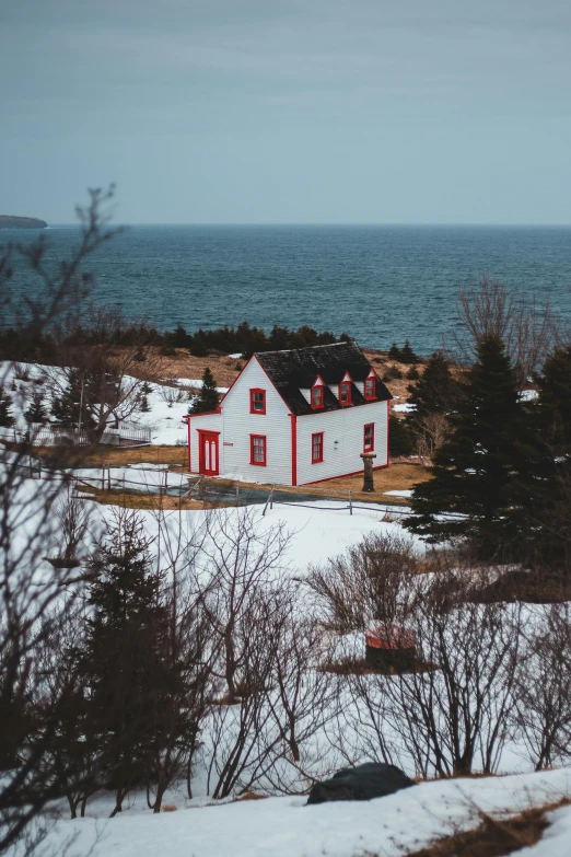 a white house sitting on top of a snow covered hill, by Daniel Seghers, pexels contest winner, views to the ocean, accents of red, farmhouse, low quality photo